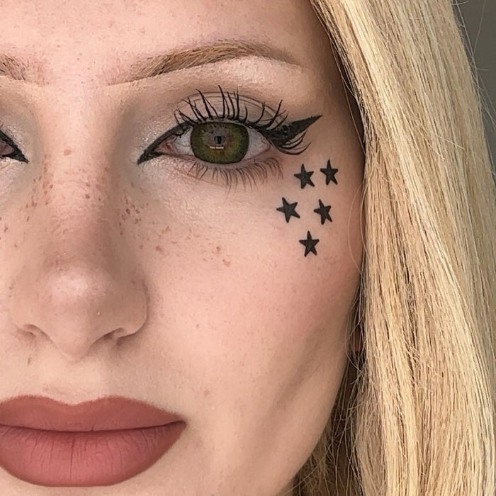 Close-up of a woman's face with star-shaped tattoos below her eye.