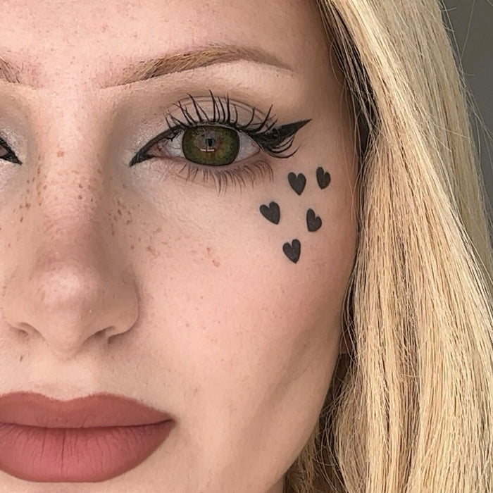 Close-up of a woman's face with heart-shaped tattoos below her eye.