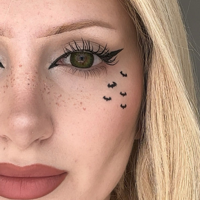 Close-up of a woman's face with small bat tattoos below her eye.