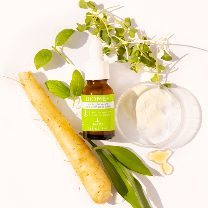 Biome+ dew bright serum travel size bottle laid in between petri dishes with ingredients and plant leaves