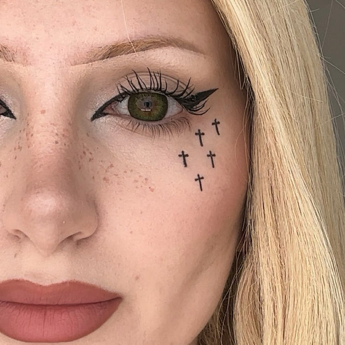 Close-up of a woman's face with small crosses tattooed below her eye.