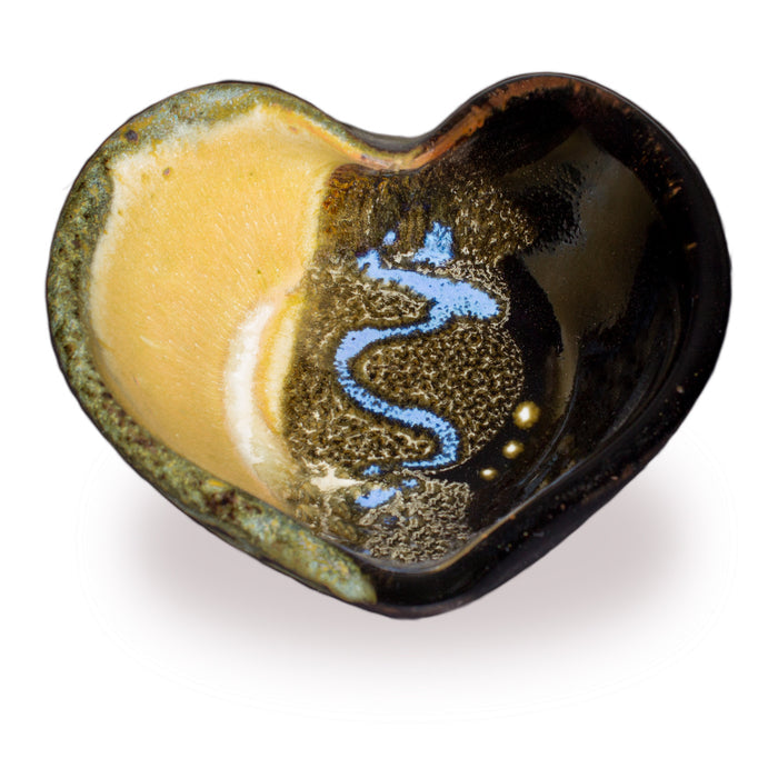 A heart-shaped ceramic bowl with a glossy finish, featuring a split design of warm yellow glaze on one side and a dark brown textured glaze with a blue wavy pattern on the other, set against a plain white background.