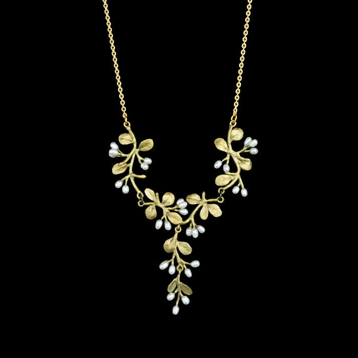 A green necklace with a leafy vine pendant featuring small white pearl-like drops, shown against a solid black background.