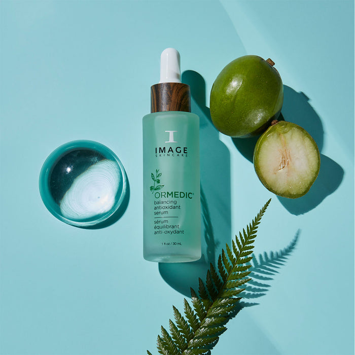 Image Skincare ORMEDIC antioxidant serum laying on blue background in between sliced fruit, plant and glass rock