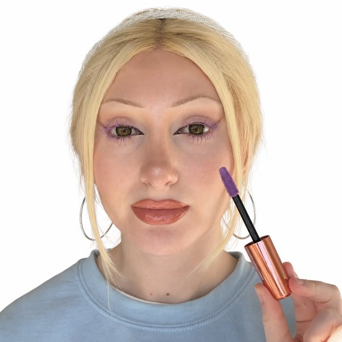 Model wearing pastel purple mascara on upper and lower lashes while holding the matching mascara wand against a white background.