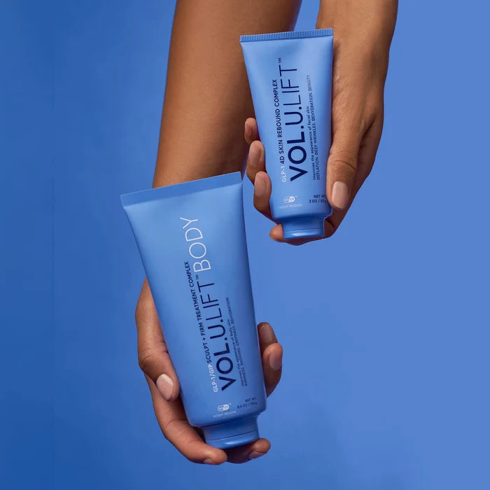 Two hands holding blue Volulift Body hand cream tubes against a solid blue background.