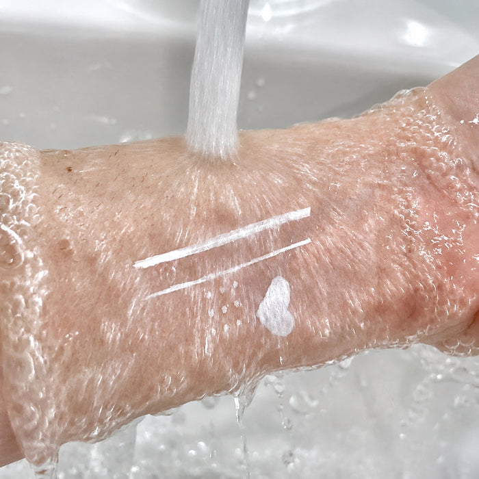 White felt-tip eyeliner lines, dots, and heart remaining visible under running water during a water-resistance test.